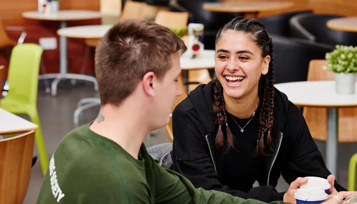 Two students chat and laugh in a cafe.